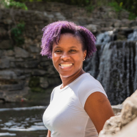 Merissa Si-Lence seated near light-colored rocks, wearing a white top, looking ahead with a calm expression. Outdoor author photo for MerissaSiLence.com