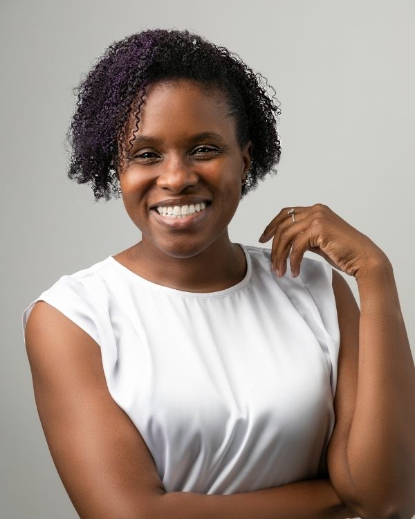 Merissa Si-Lence — Founder of rufortyfour Merissa, smiling and seated, wearing a white sleeveless top, with hand resting near her face against a light gray background.